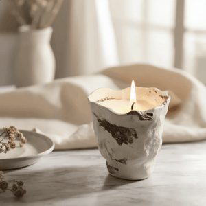Clay Pot candle holder with a lit candle on a marble surface with soft lighting